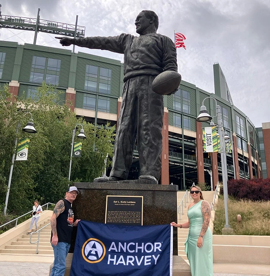 one male and female holding banner of Anchor harvey in front of a statue